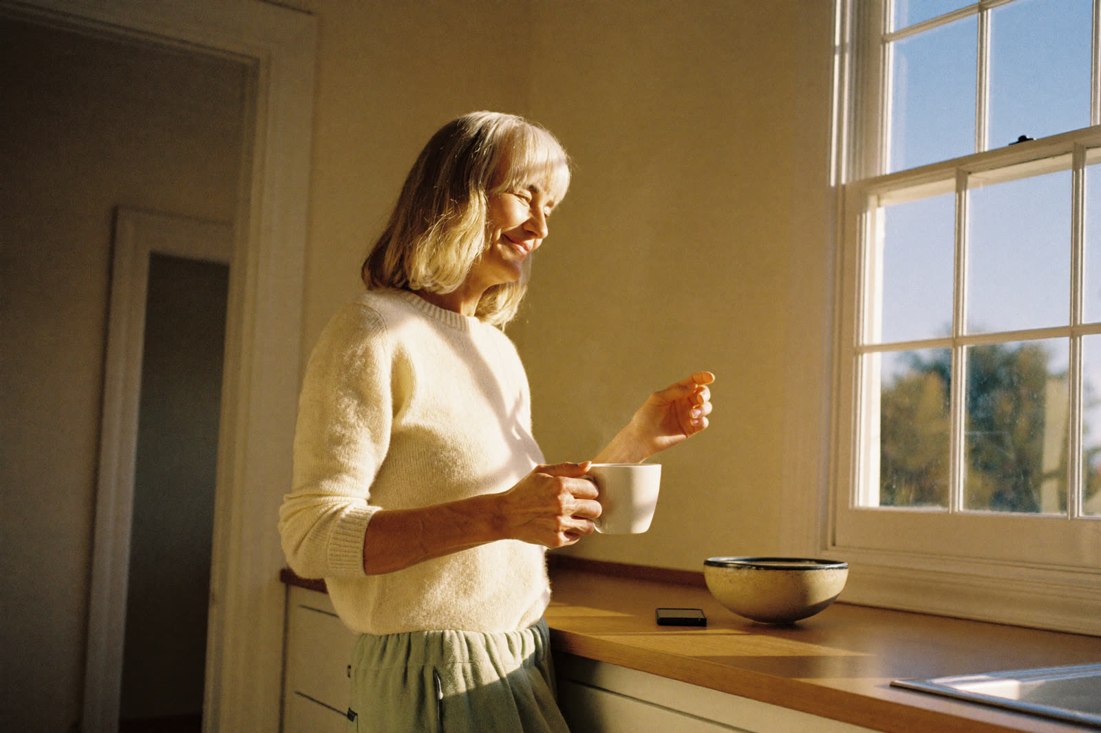 A woman in her sixties doing a gentle supported hip hinge at her kitchen counter in the morning